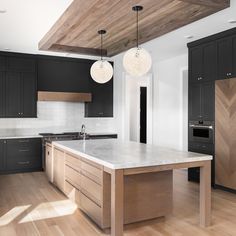 a large kitchen with black cabinets and white counter tops, wood flooring and two pendant lights hanging from the ceiling