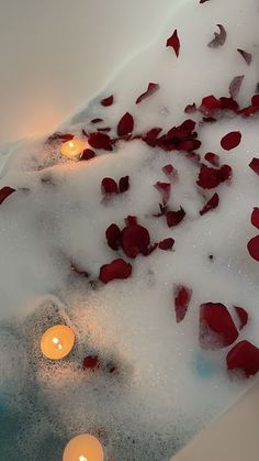 candles are floating in the water with rose petals on the floor and inside it, surrounded by foam