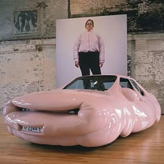 a man standing next to a pink car on top of a hard wood floor in front of a poster