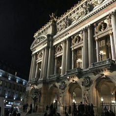 people are standing in front of an ornate building at night with lights on the side