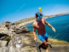 a man in swim trunks and goggles is walking near the water