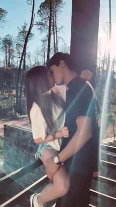 a man kissing a woman on the cheek while standing next to stairs in front of trees