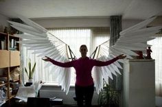 a woman standing in front of a window with large white wings on her arms and legs