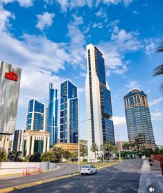 a car driving down the road in front of some tall buildings with blue sky and clouds