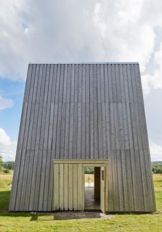 an open door in the side of a wooden building on a grassy field with blue sky and clouds