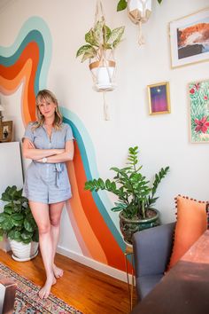 a woman standing in front of a colorful wall with potted plants on top of it