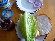 a sandwich with lettuce and onion on a plate next to a jar of jelly