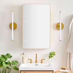 a white sink sitting under a mirror next to a wooden cabinet and potted plant