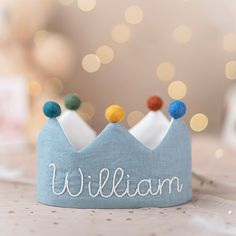 a small blue crown with the word william written on it's side and three pom - poms