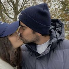 a man and woman kissing each other in front of trees with snow on the ground