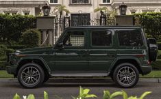 a green mercedes g - class parked in front of a large white building with palm trees