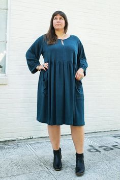 a woman standing in front of a white brick wall wearing a green dress and black boots