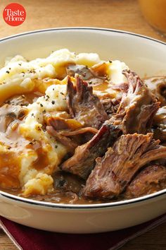 a bowl filled with meat and mashed potatoes on top of a wooden table next to a red napkin