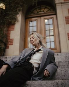 a woman sitting on the steps in front of a building wearing a suit and tie