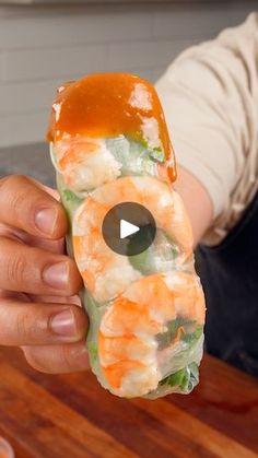 a person holding up a piece of sushi with sauce on the top and shrimp in it