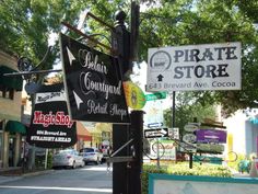 several signs are hanging on a pole in front of shops and businesses along the street