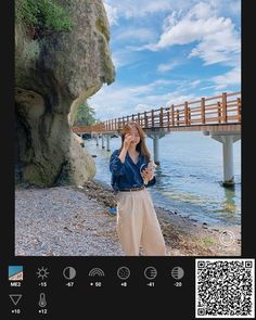 a woman standing next to a body of water holding a cell phone up to her face