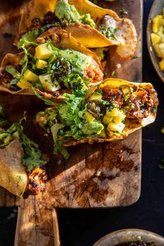 some tacos are sitting on a cutting board next to bowls of salsa and tortillas