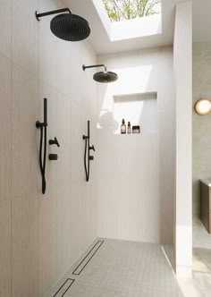 a white tiled bathroom with two shower heads and an open skylight in the ceiling