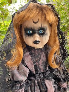 a doll with red hair and blue eyes wearing a black dress in front of some trees