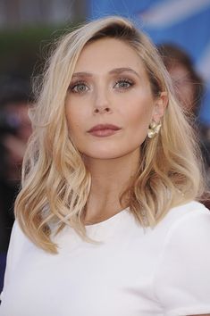 a woman with blonde hair and blue eyes is looking off to the side while wearing large earrings