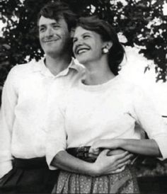 black and white photograph of two people standing next to each other with trees in the background