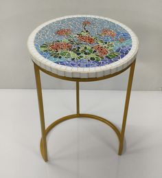 a mosaic table with gold legs and a flower design on the top, against a white background