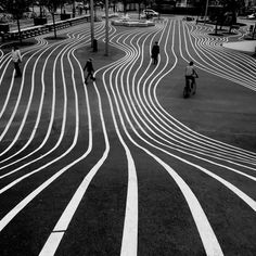 several people are walking and riding bikes on the street with white lines painted on it