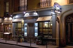 an empty street at night in front of a store with lit up windows and shutters