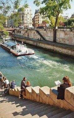 people are sitting on the steps next to the river and looking at boats in the water