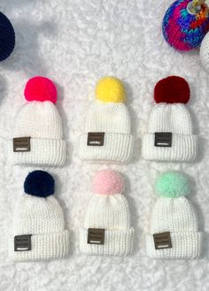 six knitted beanies with different colors and sizes on white furnishing next to two crocheted balls