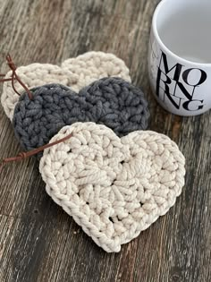 two crocheted hearts sitting next to a coffee cup