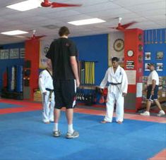 some people are standing in a room with blue and red mats on the floor while others watch