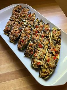 stuffed zucchini with meat and vegetables on a white platter sitting on a wooden table