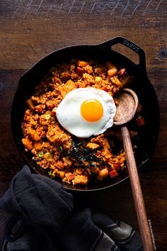 a skillet filled with food on top of a wooden table next to a spoon