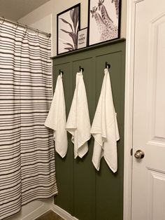 three white towels hanging on hooks in front of a green wall with black and white striped shower curtain