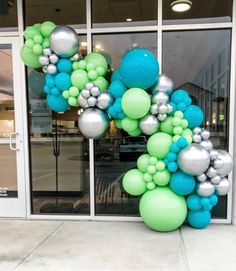 a large balloon arch in front of a building with blue, green and silver balloons