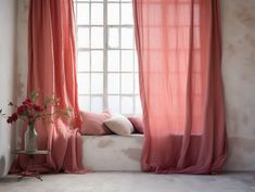 a vase with flowers sitting next to a window covered in pink drapes and curtains