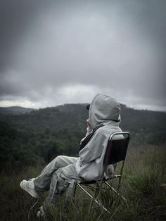 a person sitting in a chair on top of a grass covered field under a cloudy sky