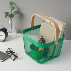 there is a green basket with some books and glasses on the table next to it