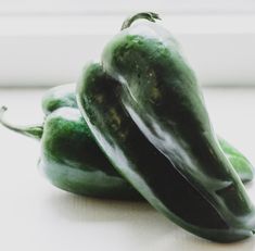 two green peppers sitting next to each other on top of a white countertop in front of a window