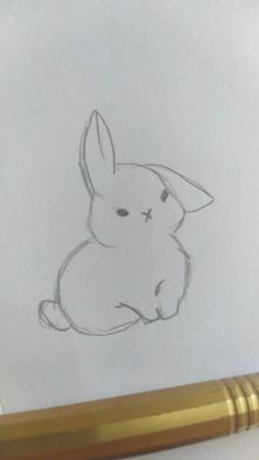 a pencil drawing of a rabbit sitting on top of a piece of paper next to a pen