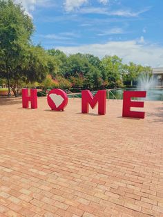 the word home is made out of red letters on a brick walkway in front of a fountain