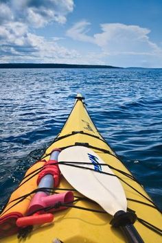 a yellow kayak with paddles is in the water near some land and blue sky