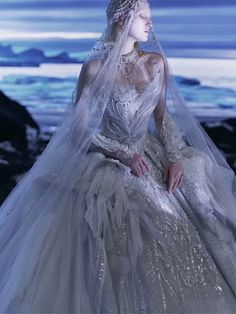 a woman in a white wedding dress sitting on the beach wearing a veil and tiara