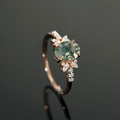 an engagement ring with a green and white stone surrounded by small diamonds on the side