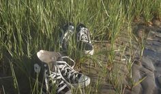 two pairs of shoes are sitting in the tall grass by the water's edge