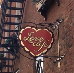 a sign that says love cafe hanging from the side of a brick building in front of a fire escape