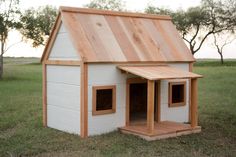 a dog house made out of wood and painted white with a wooden roof on the grass