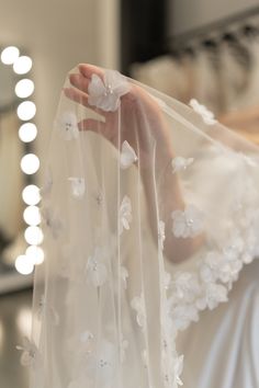 a woman in a white wedding dress is holding her veil over her shoulder with flowers on it